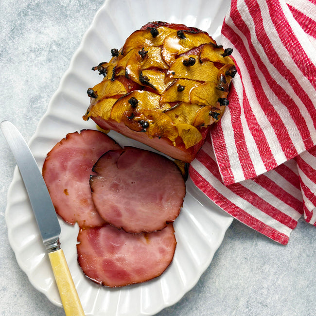 Sliced ham with apple stuffing on a white plate with a red and white striped towel.